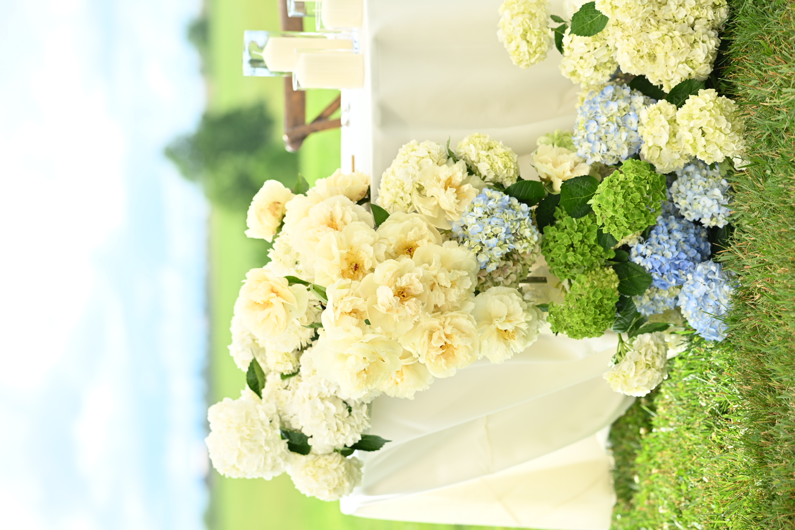 Sweetheart table with cascading cream peonies and blue and green hydrangeas overlooking pasture